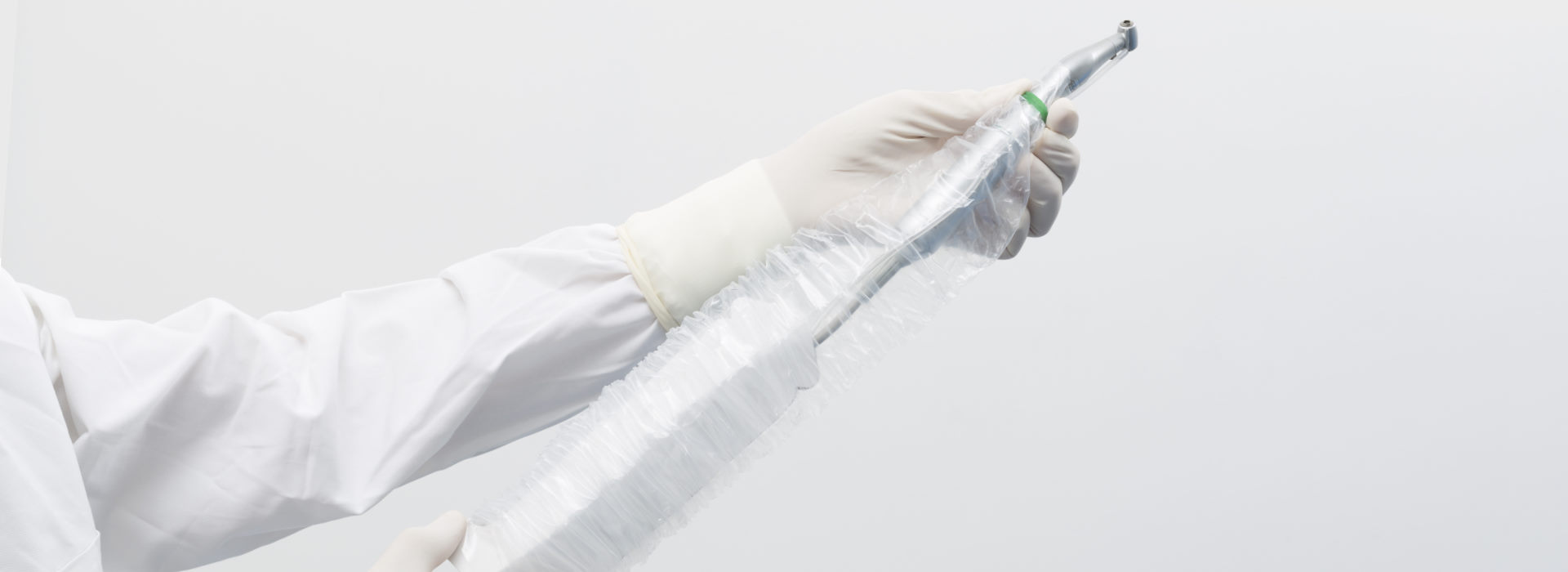 Hand in OP-Handschuhen, die einen Überzug über einen Dentalbohrer streift